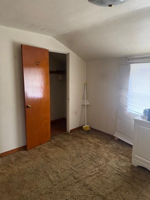 unfurnished bedroom featuring a closet, lofted ceiling, and dark colored carpet