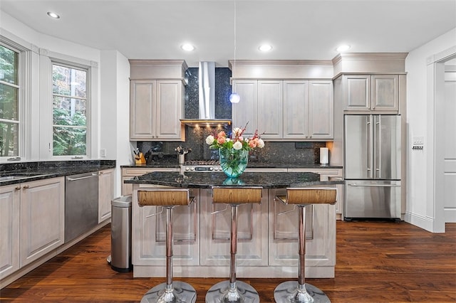 kitchen featuring wall chimney exhaust hood, a center island, appliances with stainless steel finishes, and dark stone counters