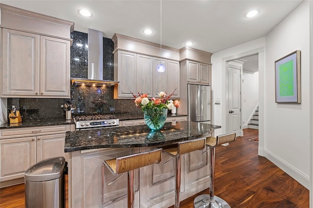 kitchen featuring tasteful backsplash, dark stone counters, wall chimney exhaust hood, stainless steel appliances, and dark wood-type flooring