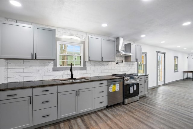 kitchen with dark hardwood / wood-style flooring, stainless steel appliances, sink, wall chimney range hood, and gray cabinets