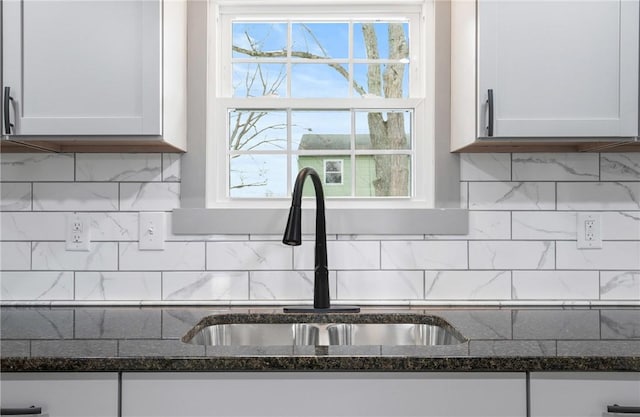 room details with white cabinets, backsplash, dark stone countertops, and sink