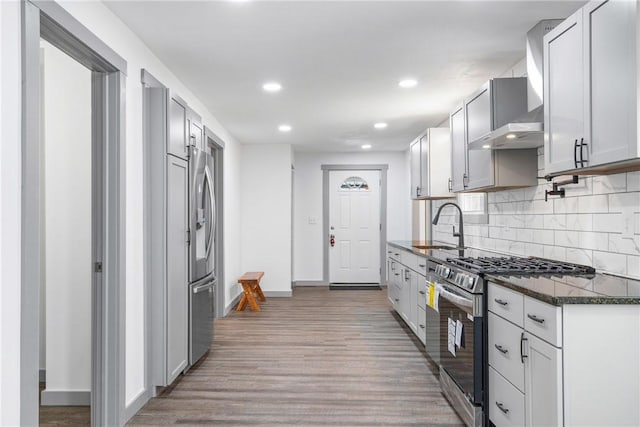 kitchen with tasteful backsplash, stainless steel appliances, sink, light hardwood / wood-style flooring, and dark stone countertops