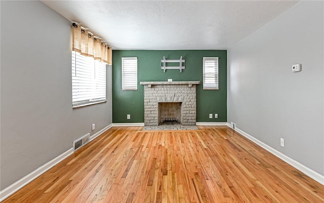 unfurnished living room featuring a healthy amount of sunlight, light wood-type flooring, and a brick fireplace