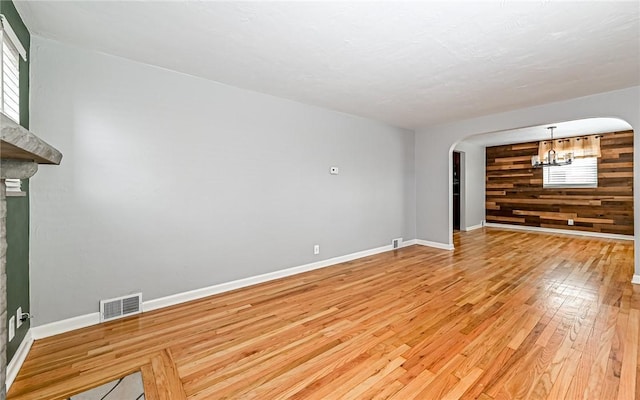 spare room featuring wood walls, light hardwood / wood-style flooring, and an inviting chandelier