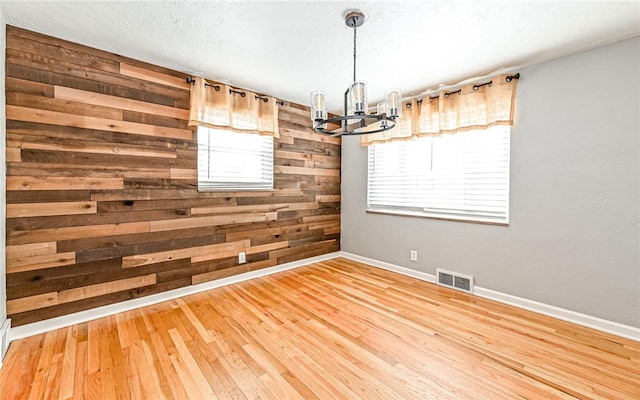 unfurnished dining area featuring a chandelier, wood-type flooring, a healthy amount of sunlight, and wood walls