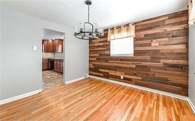 unfurnished dining area with wood walls, light hardwood / wood-style floors, and a notable chandelier