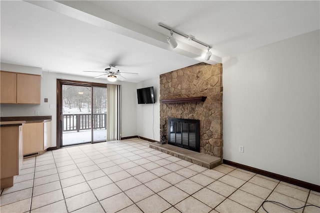 unfurnished living room featuring ceiling fan, a stone fireplace, light tile patterned floors, and rail lighting