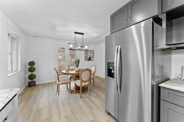 kitchen featuring light stone countertops, an inviting chandelier, stainless steel fridge with ice dispenser, light hardwood / wood-style flooring, and gray cabinets