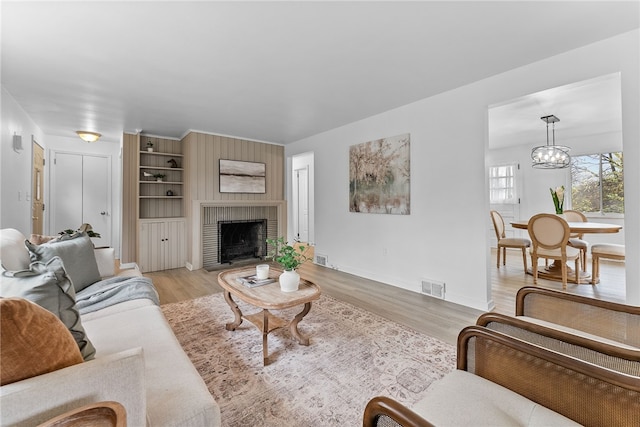 living room with light wood-type flooring, a fireplace, and an inviting chandelier