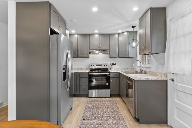 kitchen featuring stainless steel appliances, light stone counters, decorative light fixtures, gray cabinets, and light wood-type flooring