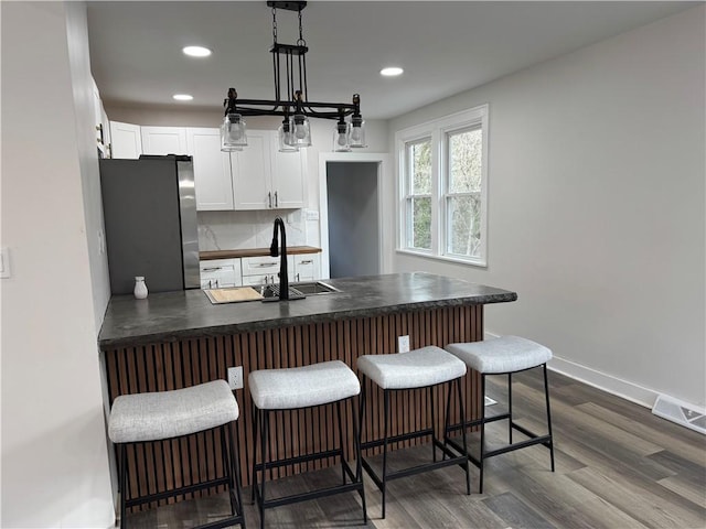 kitchen featuring a kitchen breakfast bar, dark hardwood / wood-style flooring, stainless steel fridge, decorative light fixtures, and white cabinets