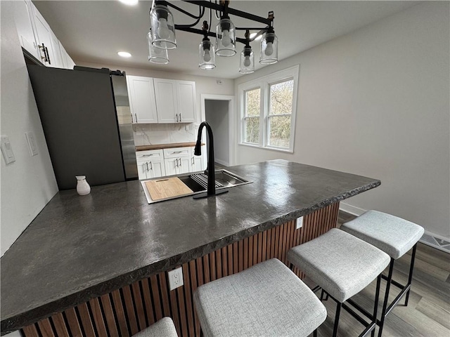 kitchen with tasteful backsplash, white cabinetry, a kitchen bar, wood-type flooring, and stainless steel refrigerator