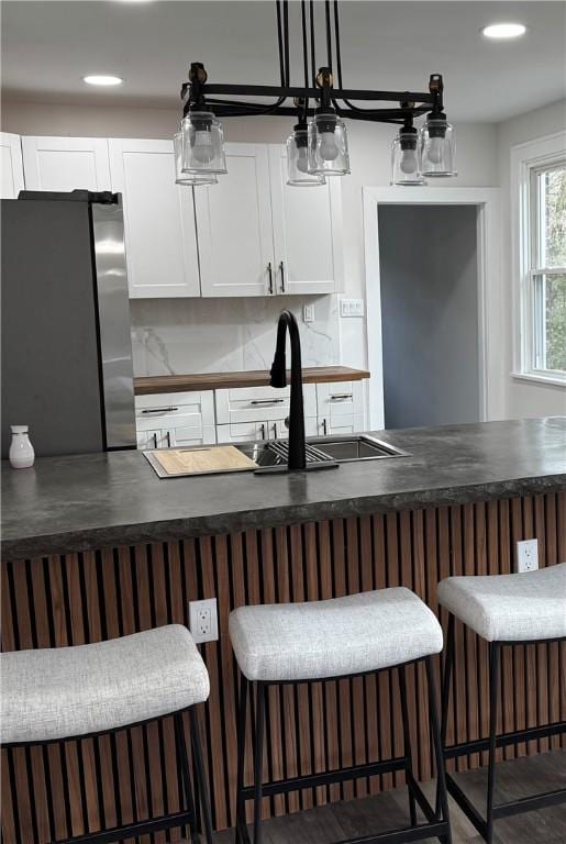 kitchen with stainless steel fridge, a kitchen breakfast bar, sink, decorative light fixtures, and white cabinetry