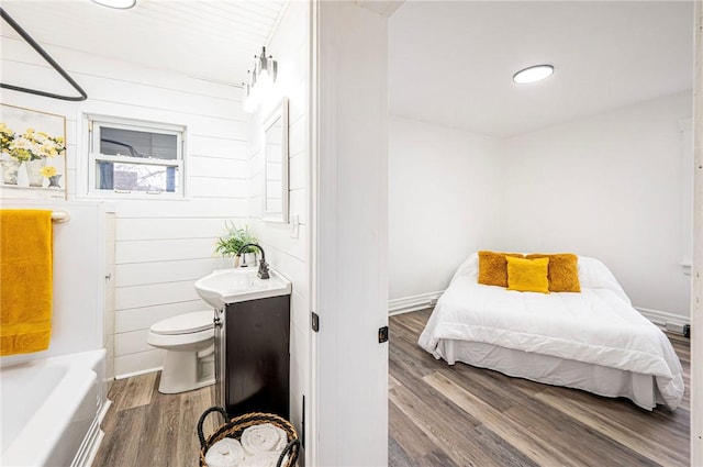 bedroom featuring wooden walls, sink, and wood-type flooring