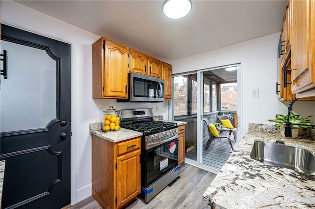 kitchen with light stone countertops, appliances with stainless steel finishes, light hardwood / wood-style floors, and sink