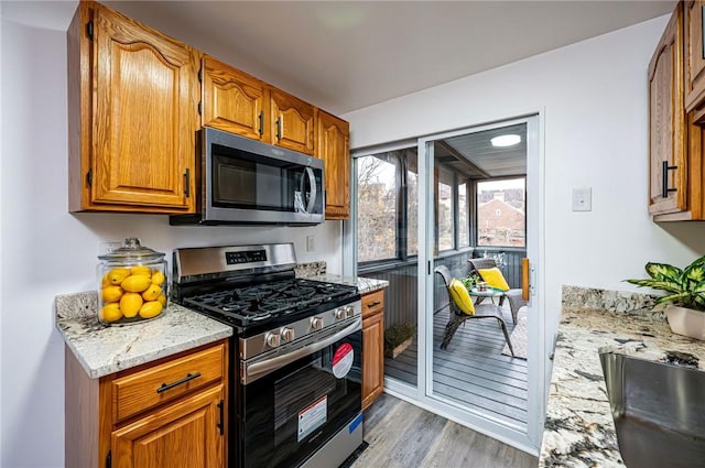 kitchen with stainless steel appliances, light stone counters, and light hardwood / wood-style floors