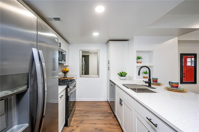 kitchen with light stone countertops, white cabinetry, sink, appliances with stainless steel finishes, and light wood-type flooring