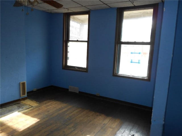 spare room featuring a drop ceiling, dark hardwood / wood-style floors, a wealth of natural light, and ceiling fan