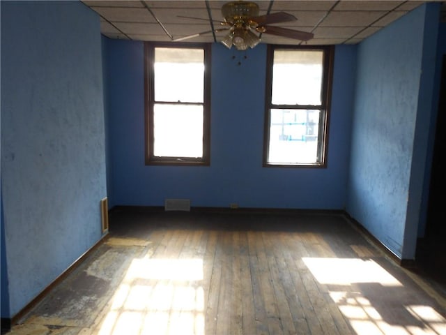 empty room with dark hardwood / wood-style flooring, a drop ceiling, and ceiling fan