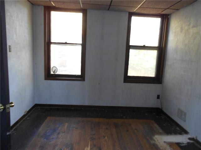 spare room with plenty of natural light, a drop ceiling, and dark wood-type flooring