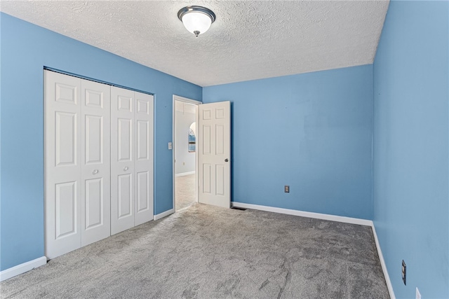 unfurnished bedroom with light colored carpet, a textured ceiling, and a closet