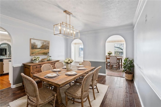 dining room with a textured ceiling, dark wood-type flooring, crown molding, and a notable chandelier