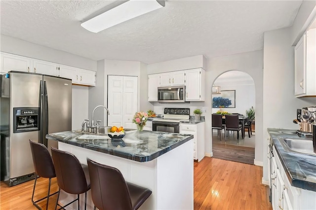 kitchen with a textured ceiling, appliances with stainless steel finishes, a kitchen island, white cabinetry, and light hardwood / wood-style flooring