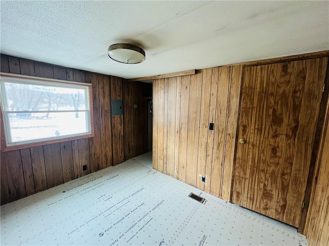 unfurnished room with visible vents, wood walls, light colored carpet, electric panel, and a textured ceiling