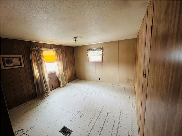 empty room with wooden walls, visible vents, and a textured ceiling