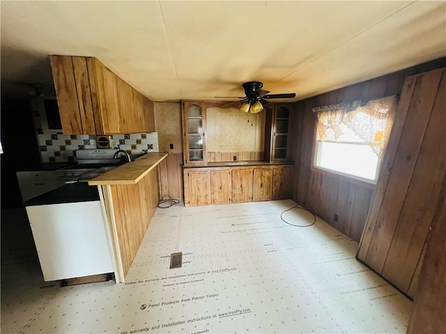 kitchen featuring a ceiling fan, light floors, stove, brown cabinets, and backsplash