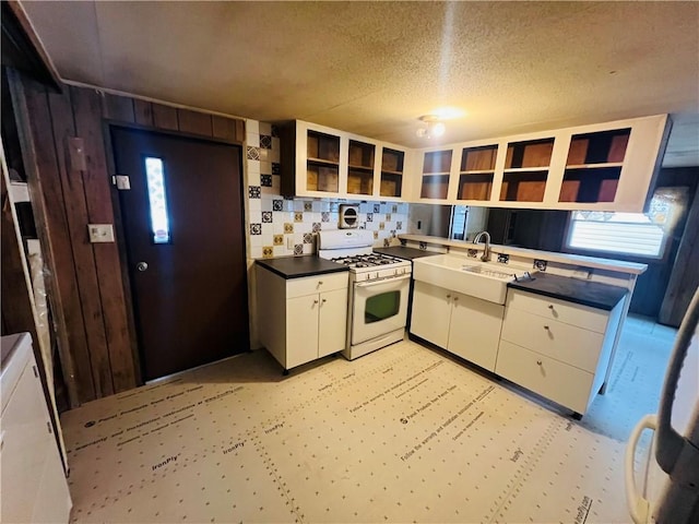 kitchen featuring dark countertops, open shelves, gas range gas stove, white cabinets, and a sink