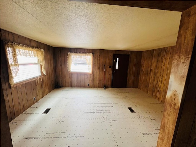 spare room with wooden walls, visible vents, and a textured ceiling