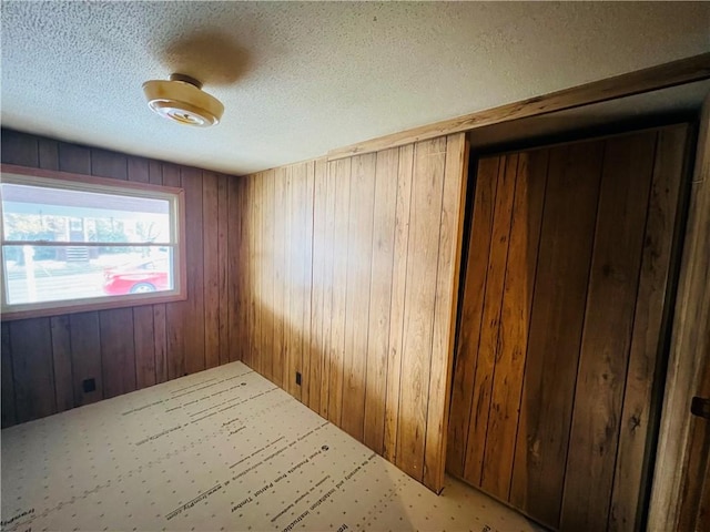 carpeted empty room with wooden walls and a textured ceiling