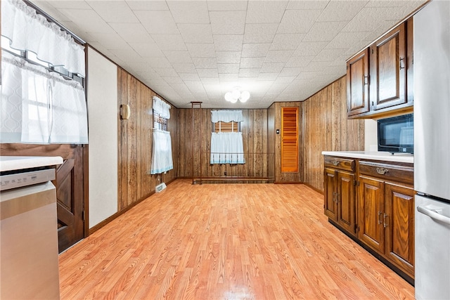 kitchen with stainless steel fridge, light hardwood / wood-style floors, wooden walls, and a healthy amount of sunlight