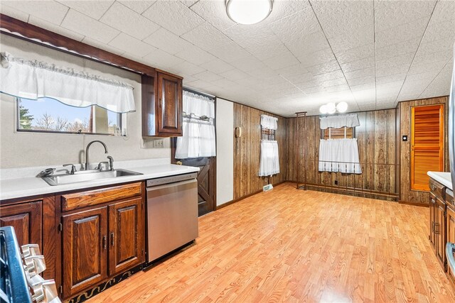 kitchen with stainless steel dishwasher, wood walls, light hardwood / wood-style floors, and sink