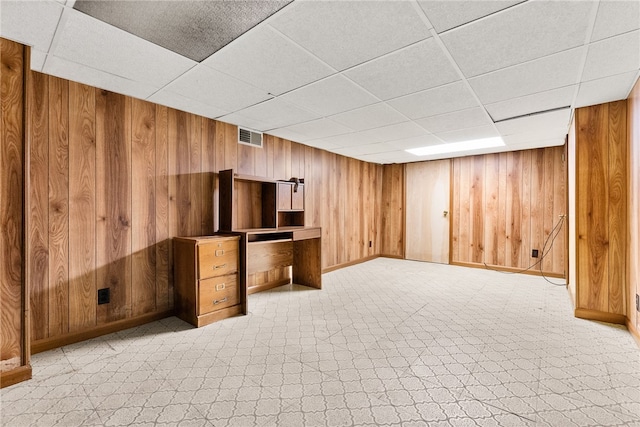 basement featuring a drop ceiling and wooden walls