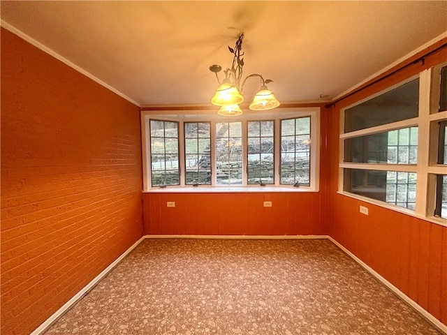 unfurnished dining area featuring a notable chandelier, wood walls, and ornamental molding