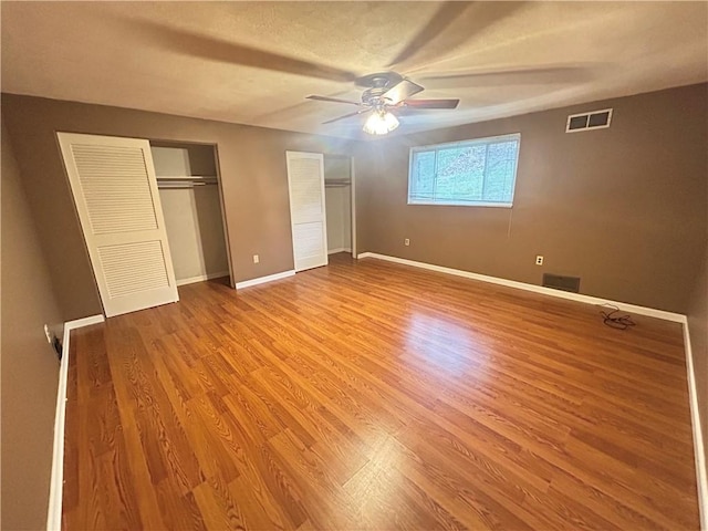 unfurnished bedroom with ceiling fan, wood-type flooring, and multiple closets