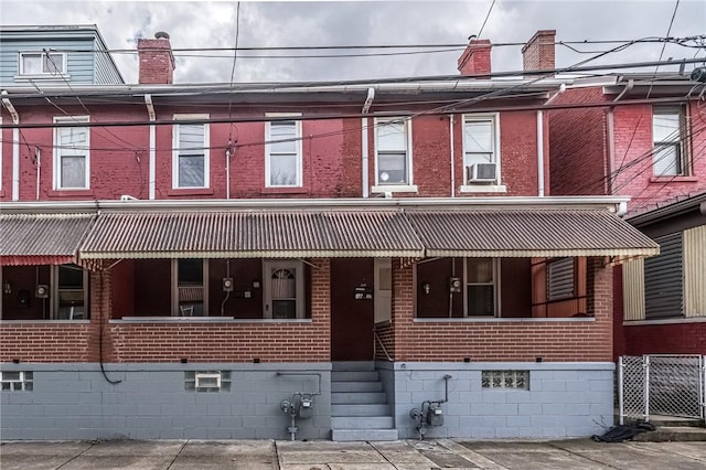 view of property with covered porch, brick siding, and a chimney