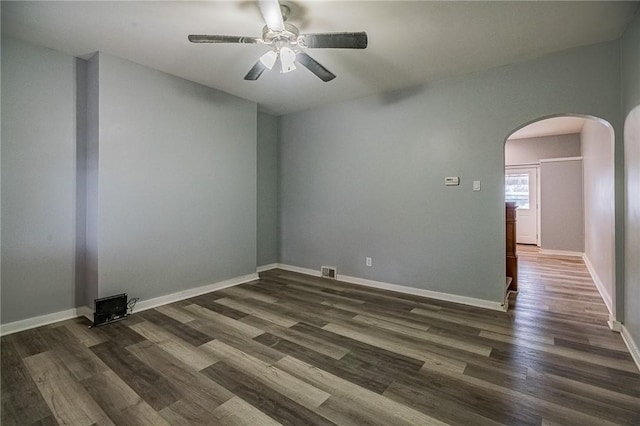 empty room with dark wood-style floors, arched walkways, visible vents, ceiling fan, and baseboards