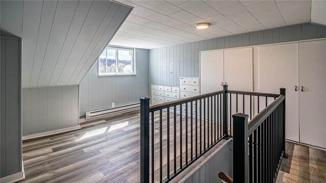 additional living space featuring wooden walls, a baseboard radiator, vaulted ceiling, and hardwood / wood-style flooring