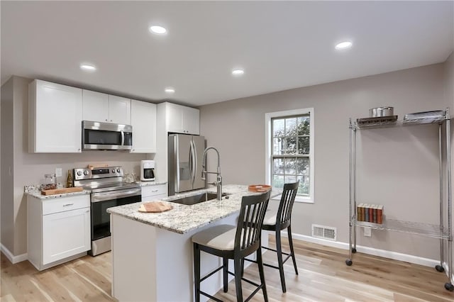 kitchen featuring appliances with stainless steel finishes, sink, light hardwood / wood-style floors, white cabinetry, and an island with sink