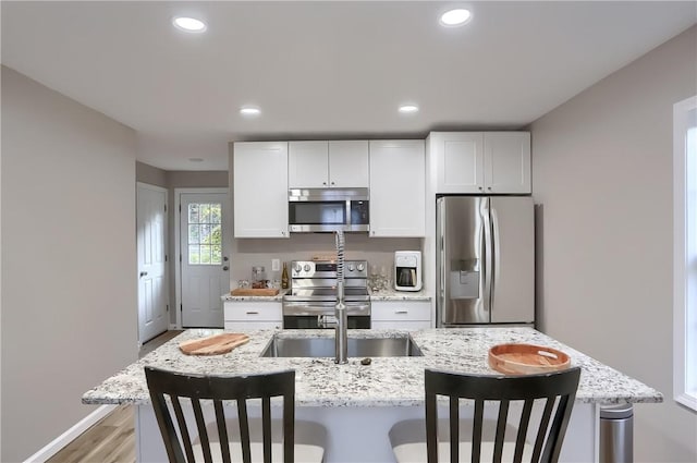 kitchen featuring a kitchen breakfast bar, light hardwood / wood-style flooring, white cabinets, and appliances with stainless steel finishes