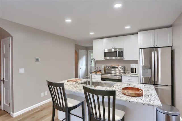 kitchen with light stone countertops, appliances with stainless steel finishes, an island with sink, white cabinets, and light wood-type flooring