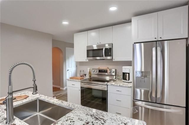 kitchen featuring sink, hardwood / wood-style flooring, light stone countertops, appliances with stainless steel finishes, and white cabinetry