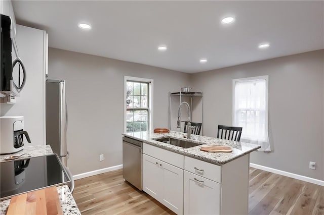 kitchen featuring white cabinets, a center island with sink, sink, light hardwood / wood-style flooring, and appliances with stainless steel finishes