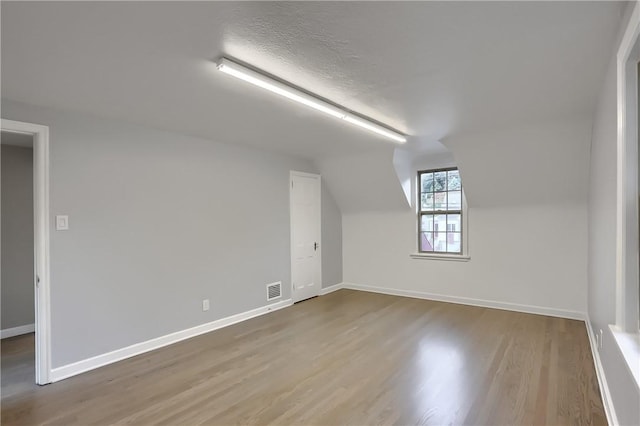 bonus room with wood-type flooring, a textured ceiling, and vaulted ceiling