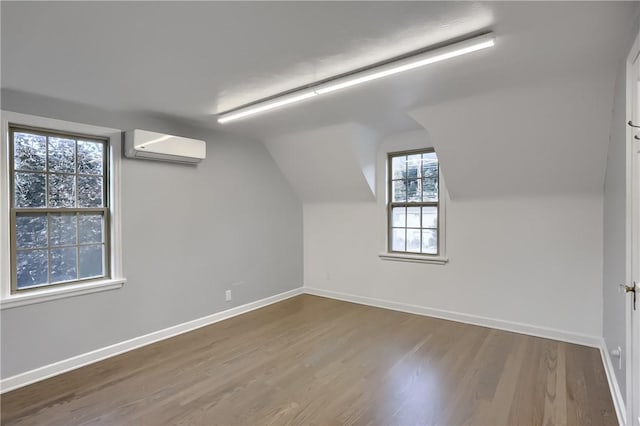 additional living space featuring a wall mounted air conditioner, wood-type flooring, and vaulted ceiling