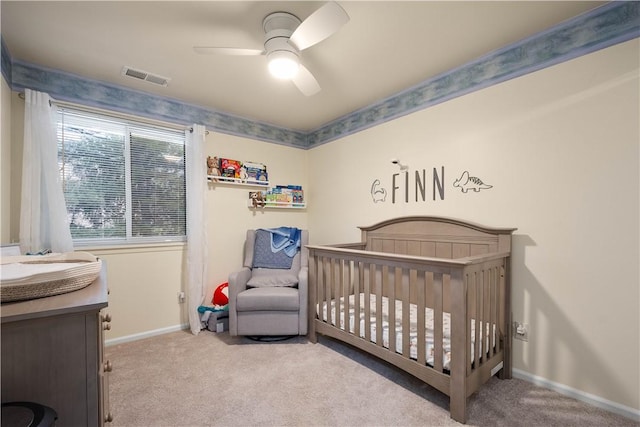 carpeted bedroom with ceiling fan and a nursery area