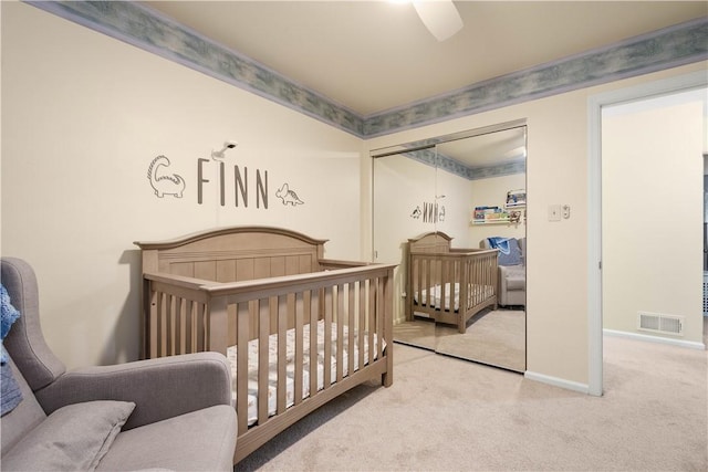 carpeted bedroom featuring a nursery area, a closet, and ceiling fan